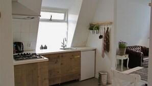 Una cocina con encimera de madera, un fregadero y una ventana. Hay un cubo de basura y una mesita con una planta.