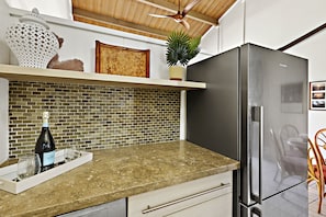 Una cocina con encimera de mármol, refrigerador de acero inoxidable, una planta en maceta y una botella de vino sobre la encimera.