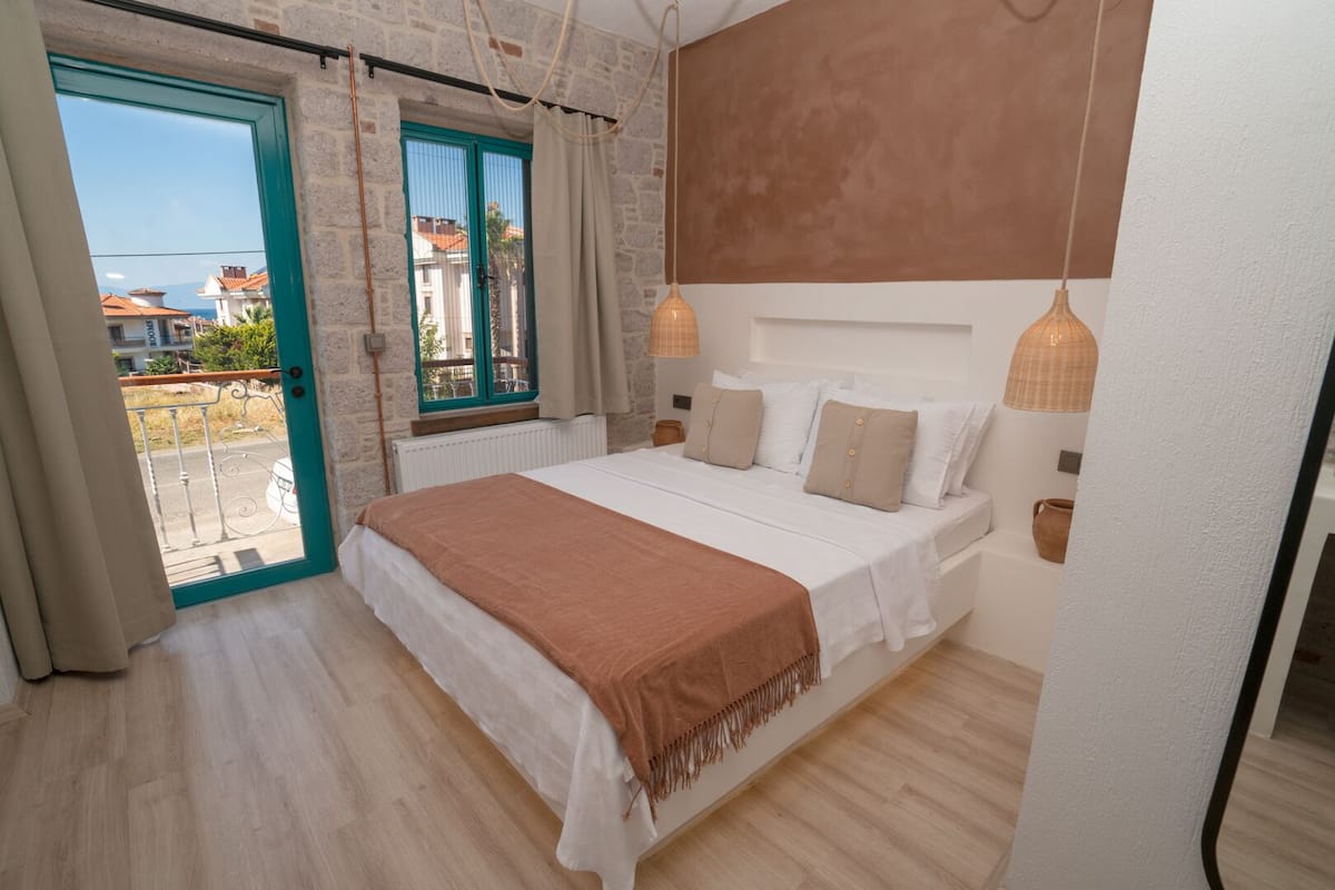 A bedroom with a bed, a window with curtains, a view of the outside, and a hanging light fixture.
