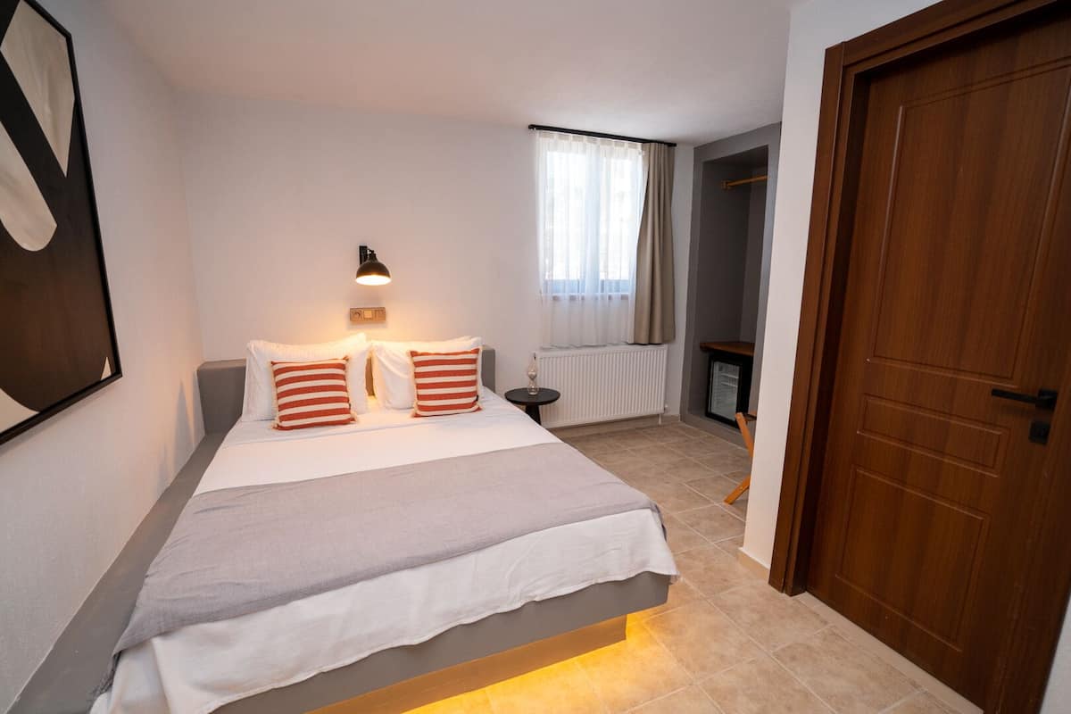 A bedroom with a bed, bedside table, lamp, and a view of a hallway.