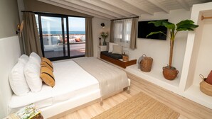 Un dormitorio con una cama grande, una mesita de noche pequeña, una planta en maceta y vistas al mar.