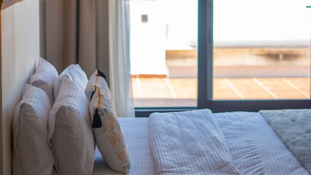 Un dormitorio con cama, almohadas, una lámpara de noche y vistas al mar a través de un ventanal grande.