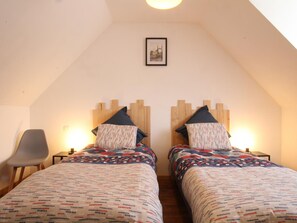 Une chambre avec deux lits, chacun agrémenté de draps à motifs et d’une tête de lit en bois. Un tableau encadré est accroché au mur, au-dessus des lits.