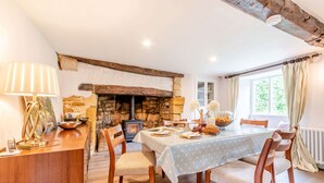 Un comedor con chimenea de piedra, sillas de madera, una mesa lista para dos comensales y una lámpara.
