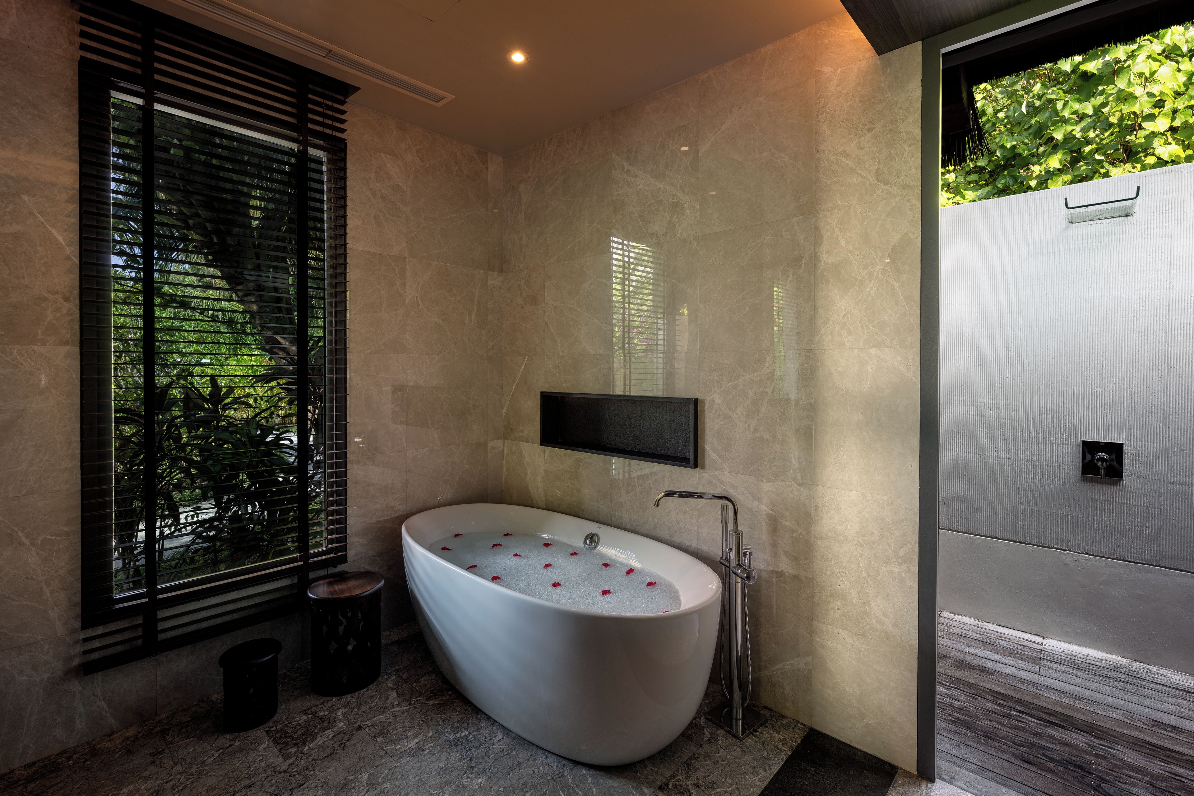 Ein modernes Badezimmer mit freistehender Badewanne, einem am Wand montierten Fernseher und einem Fenster mit Jalousien.