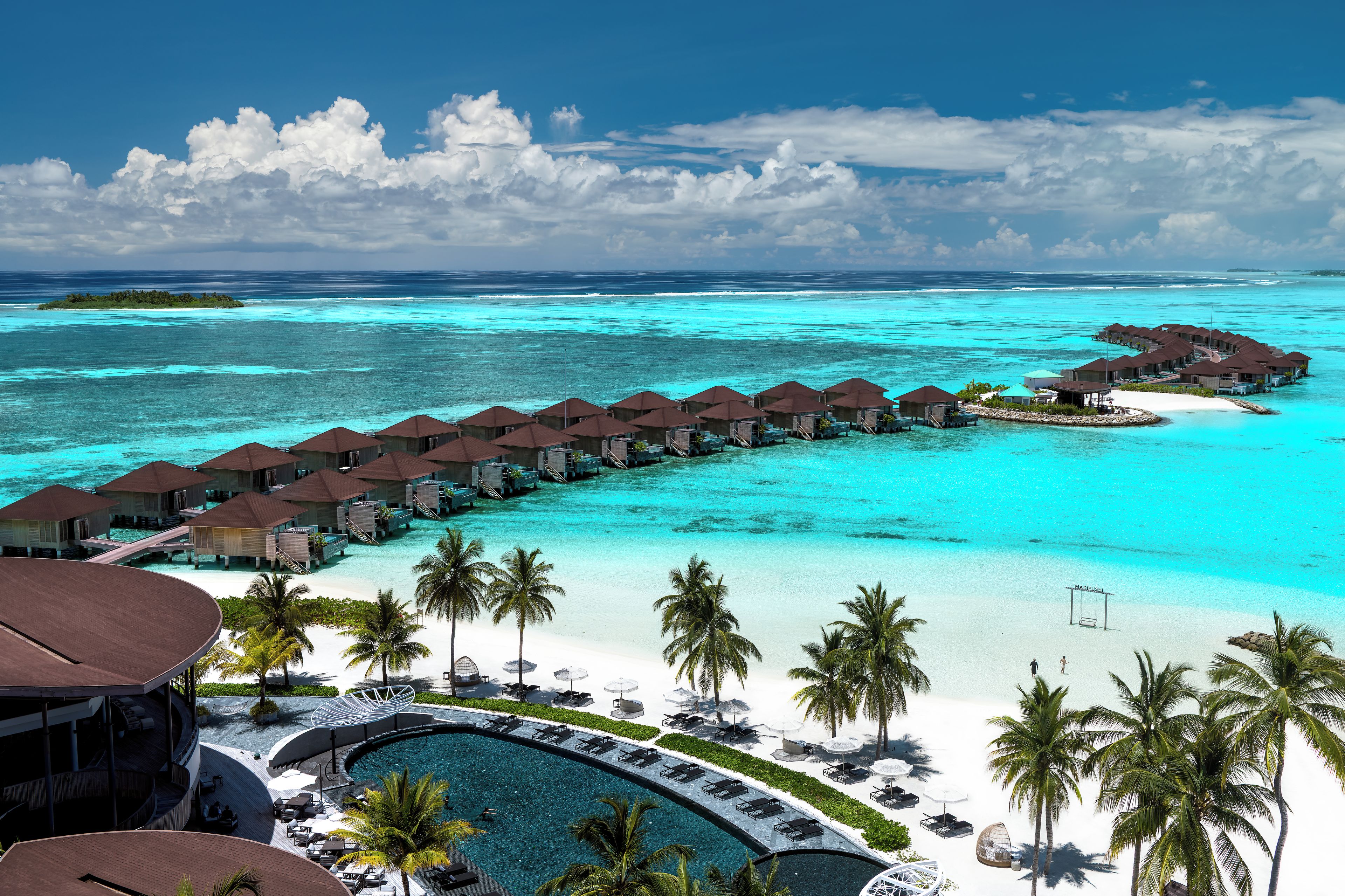 Un resort con bungalows sobre el agua unidos por pasarelas, un área de piscina y una playa.