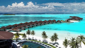 Un resort con bungalows sobre el agua unidos por pasarelas, un área de piscina y una playa.