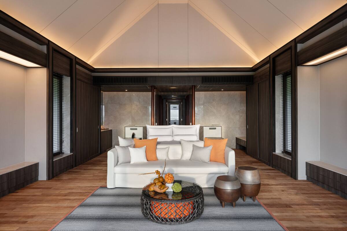 A modern living room with a white sofa, orange cushions, a glass coffee table with fruit, and wooden accents.