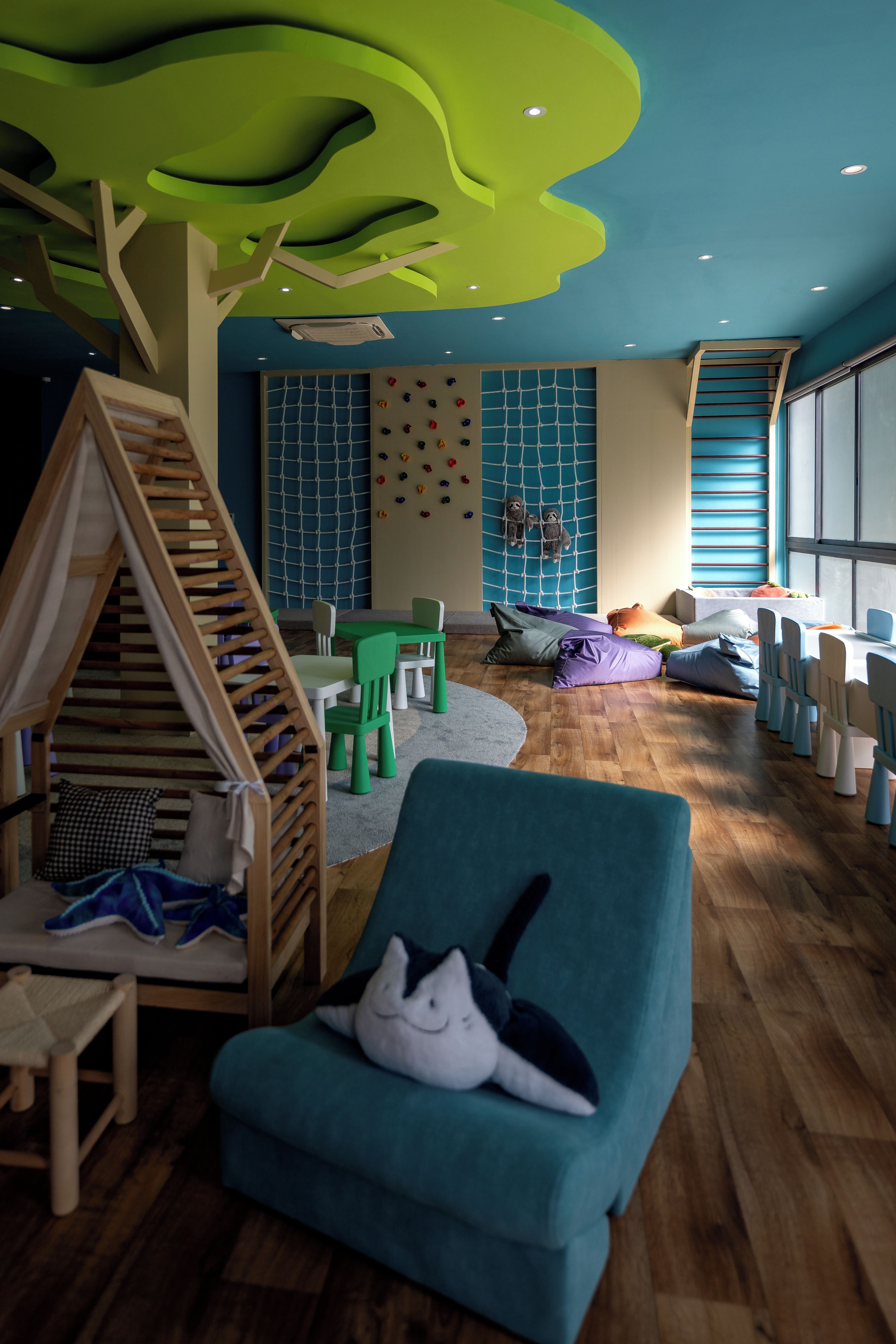 A children's playroom with a wooden playhouse, green chairs, and a blue sofa.