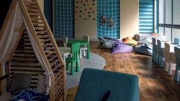 A children's playroom with a wooden playhouse, green chairs, and a blue sofa.