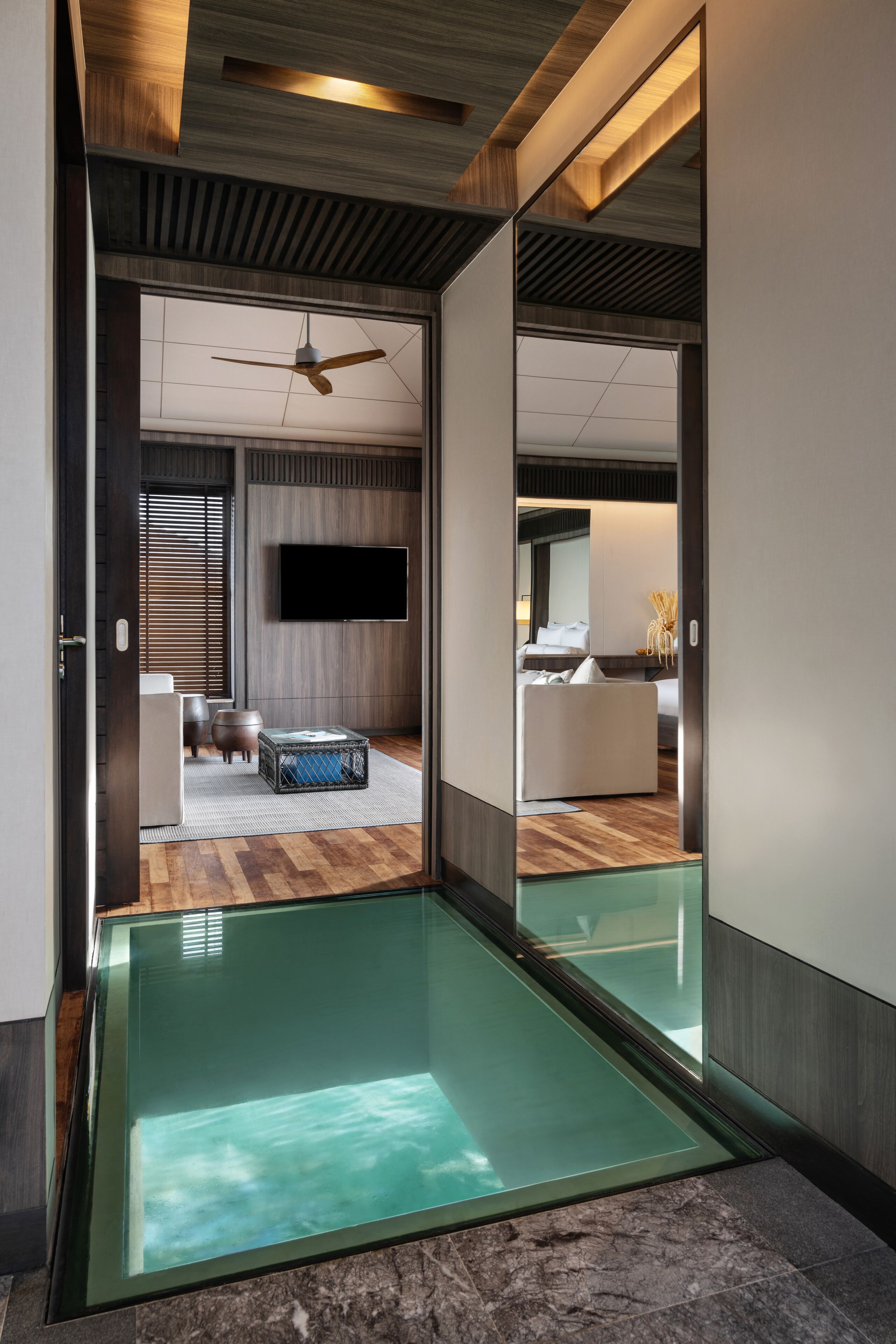 A modern hotel room with a glass floor, wooden ceiling, and a flat-screen TV mounted on the wall.
