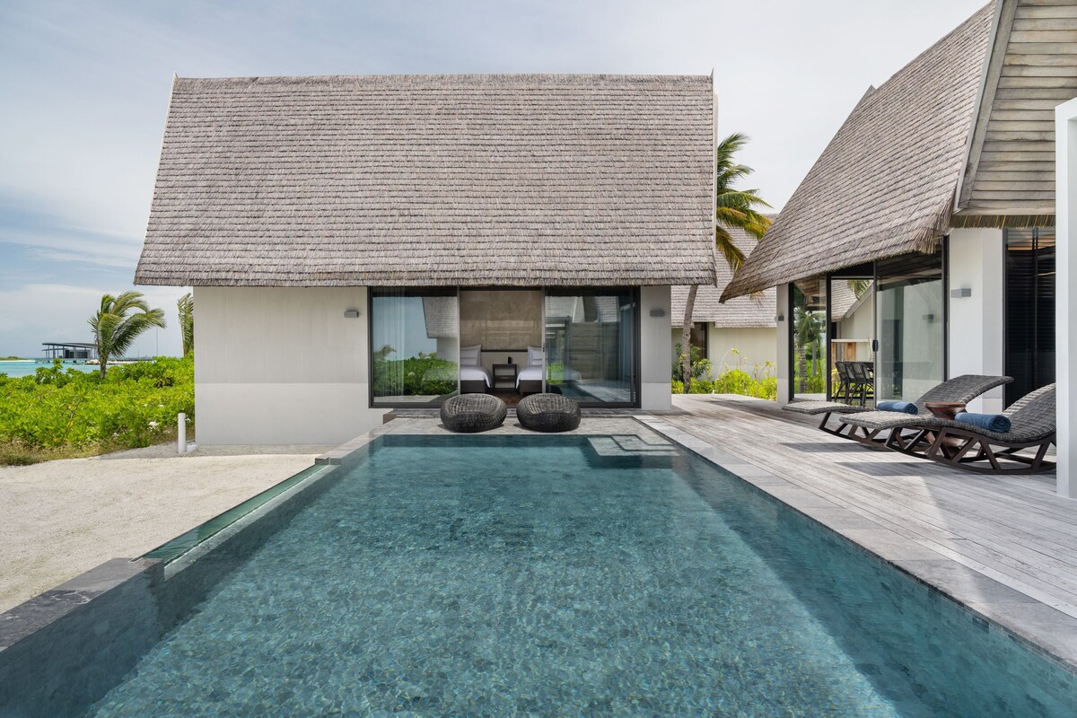 Un resort moderno con piscina, sillas de descanso y una construcción con techo de paja.