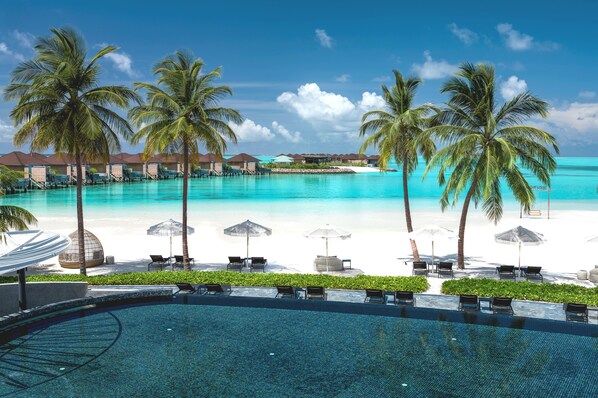 A resort with a swimming pool, beach, and overwater bungalows.