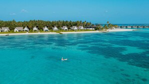 An aerial view of a resort with overwater bungalows, clear turquoise water, and a sandy beach.