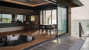 A modern interior with a dining area, kitchen, and a large window overlooking the sea.