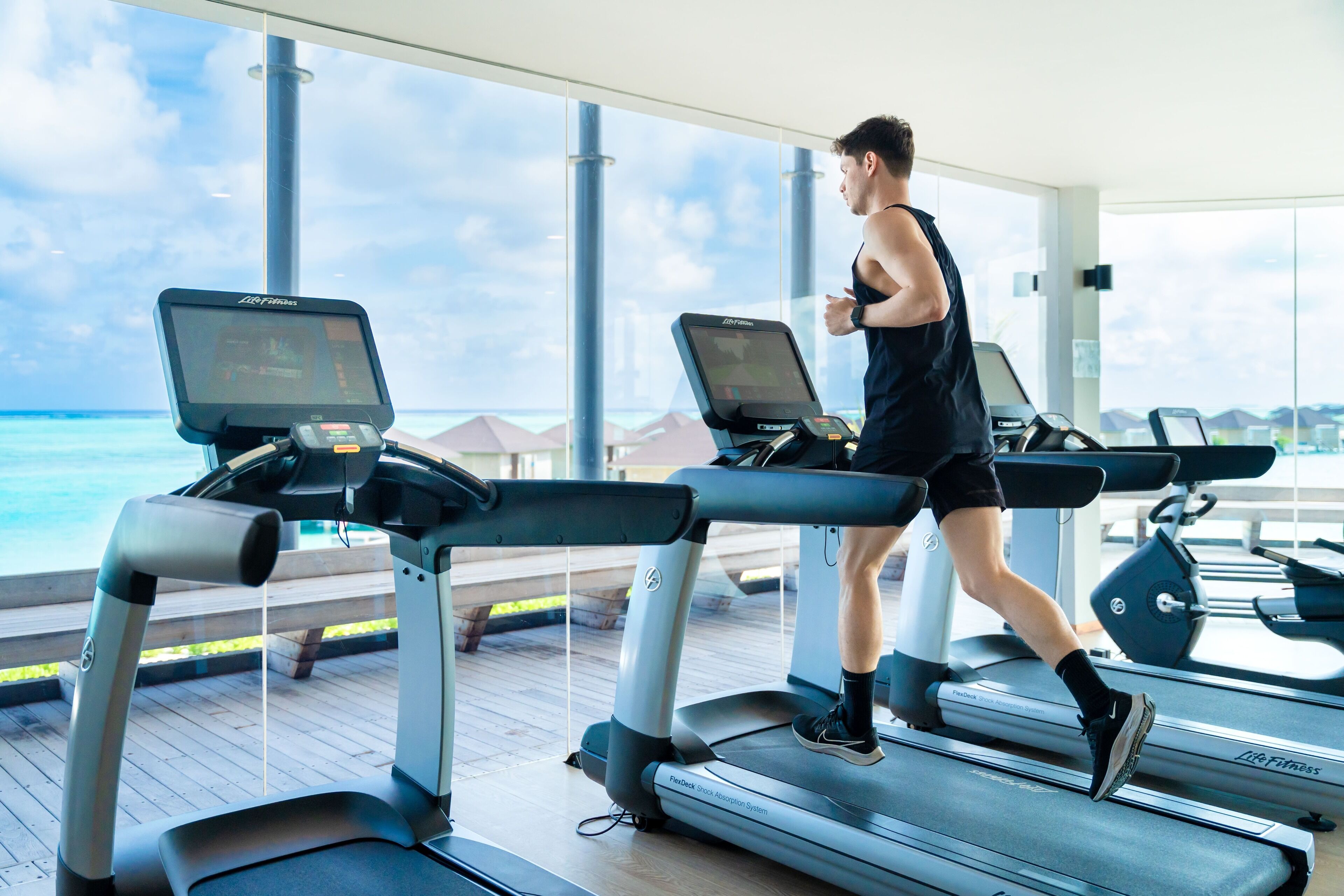 A person running on a treadmill with a view of the ocean through large windows.