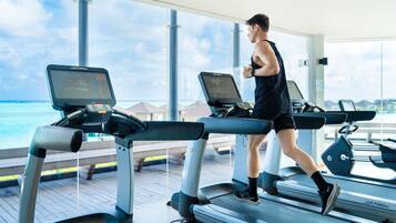 A person running on a treadmill with a view of the ocean through large windows.