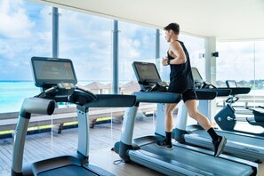 A person running on a treadmill with a view of the ocean through large windows.