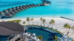An aerial view of a resort with overwater bungalows, a pool, and a beach area.
