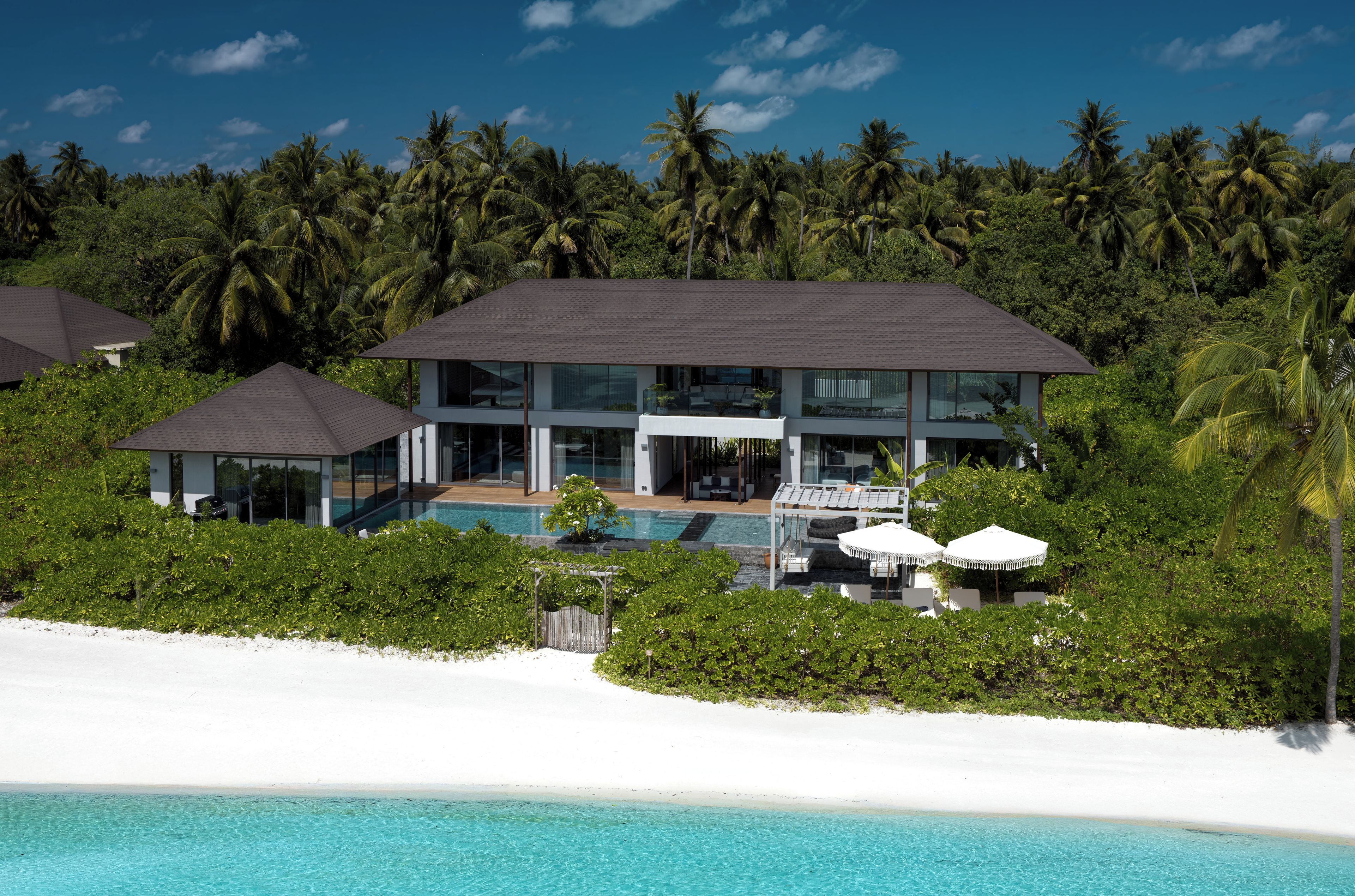Un moderno resort con piscina, playa de arena blanca y exuberante vegetación tropical.