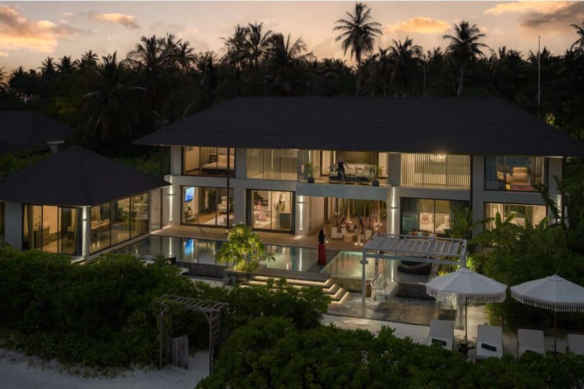 A modern two-story house with a swimming pool, surrounded by lush greenery and palm trees.