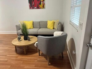 Relax in this inviting living space with a sofa, armchair, and coffee table, surrounded by a vibrant abstract art piece and a potted plant.