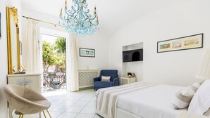 A bedroom with a bed, a chair, a TV, and a chandelier. - Queen Suite (Forio)