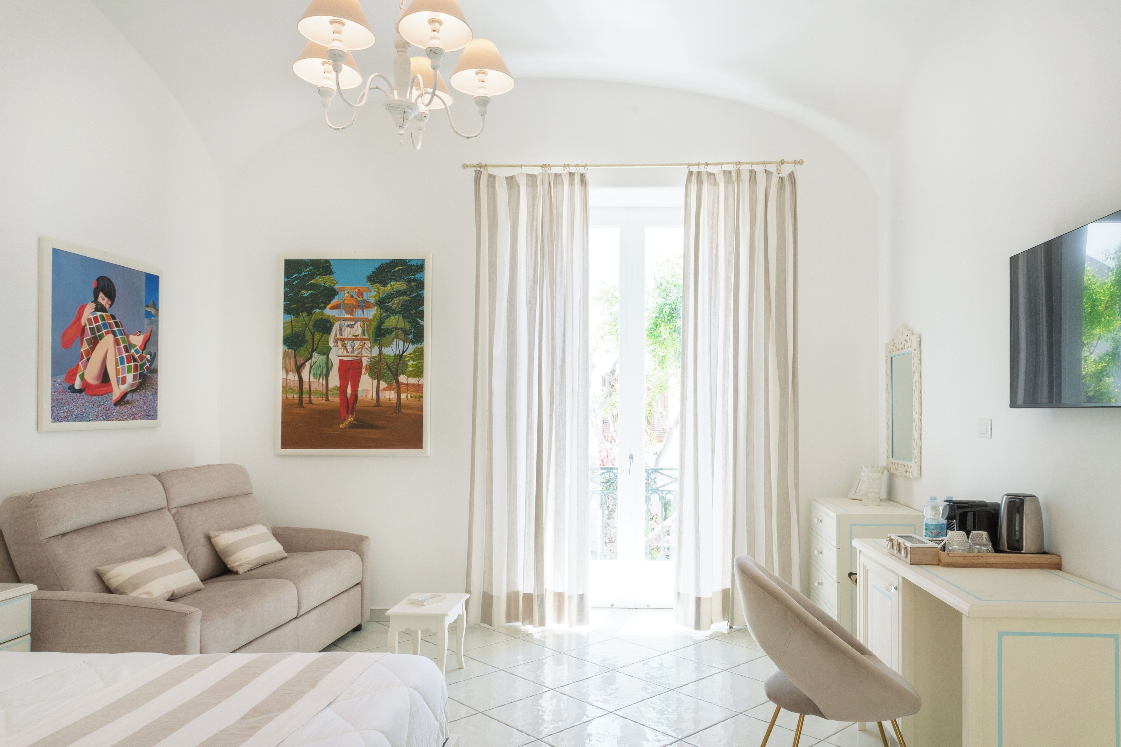 Une chambre à coucher comprenant un lit, un canapé, une chaise, un bureau, une télévision et des œuvres d’art accrochées aux murs.
