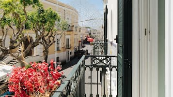 Een smalle straat met gebouwen aan weerszijden, een boom met rode bloemen op de voorgrond en een balkon met een metalen hekwerk.