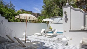 A rooftop pool area with lounge chairs and umbrellas, a small pool, and a white wall with decorative elements. - Queen Suite (Forio)