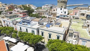 A coastal town with historic architecture, including a prominent tower, and a central square with a fountain. - Queen Suite (Forio)