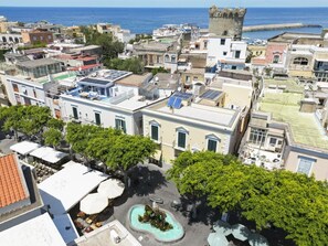 A coastal town with historic architecture, including a prominent tower, and a central square with a fountain. - Queen Suite (Forio)