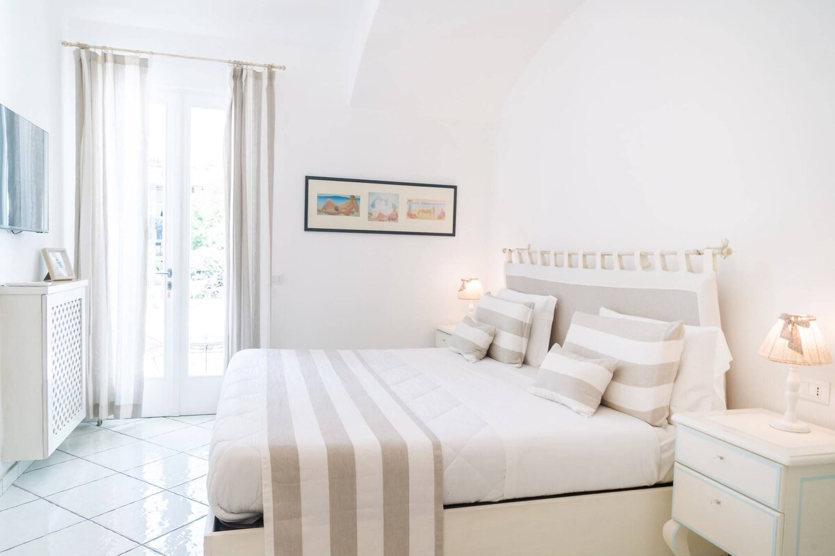 A bedroom with a bed, bedside tables, a lamp, a framed picture on the wall, and a window with curtains.