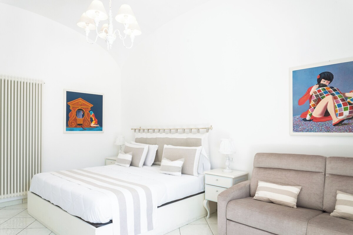 A bedroom with a bed, a nightstand, a sofa, and two wall-mounted paintings.