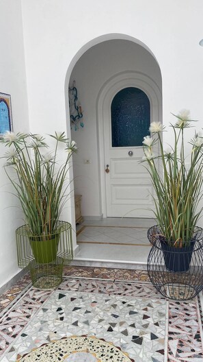 A white door with a blue glass window, flanked by two potted plants with white flowers. - Queen Suite (Forio)