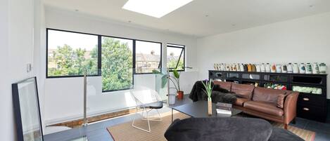 Un salon moderne avec une cloison en verre, un canapé en cuir marron, un fauteuil noir et une plante en pot.