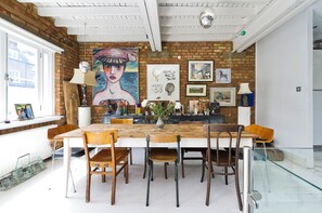 Uma área de refeições com parede de tijolos, obras de arte e uma mesa de vidro.