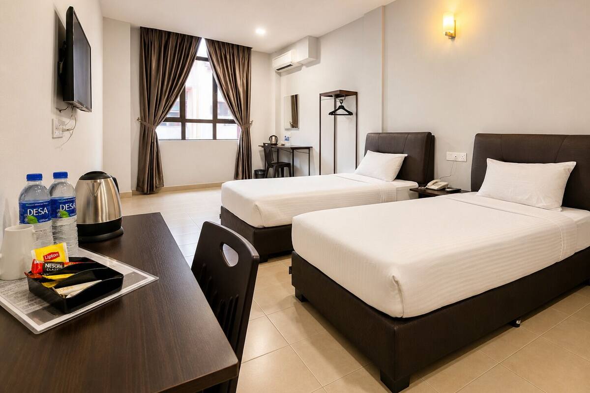 Habitación de hotel con dos camas, un escritorio con hervidor, botellas de agua, cafetera y televisor.