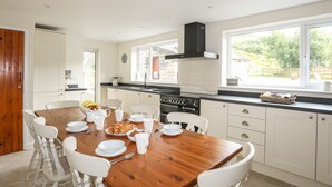 A modern kitchen with white cabinetry, a wooden dining table, and a large window offering a view of the outdoors.