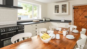 A modern kitchen with white cabinetry, a black stove, and a wooden dining table set for breakfast.
