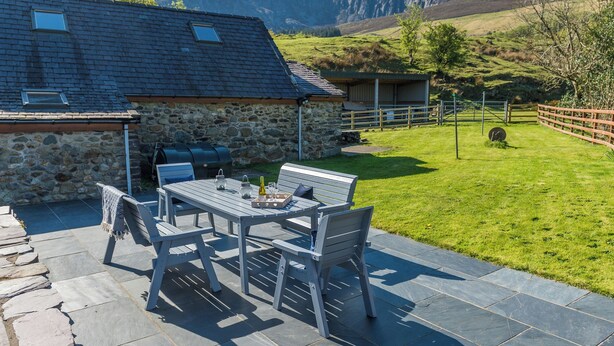 A stone house with a patio table and chairs, a barbecue, and a view of mountains.