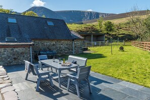 A stone house with a patio table and chairs, a barbecue, and a view of mountains. - Ty Coch (Caernarfon)