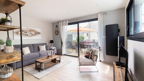 Una sala de estar moderna con sofá, mesa de centro y televisión. Cuenta con un balcón y mobiliario exterior.