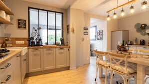 Una cocina moderna con armarios de madera, un comedor con mesa y sillas blancas, y un ventanal que proporciona luz natural.