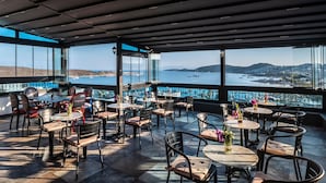 An outdoor dining area with tables and chairs, overlooking a body of water and distant hills. - Art & Interiors (Bodrum)