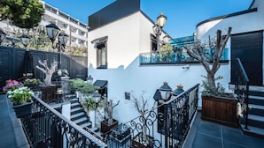 A courtyard with a staircase, potted plants, and a white building with black railings and a blue balcony. - Art & Interiors (Bodrum)