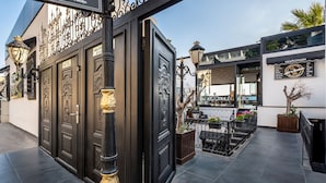 A hotel entrance with ornate black doors, a wrought iron gate, and a sign for 'Art Interiors' on the right. - Art & Interiors (Bodrum)