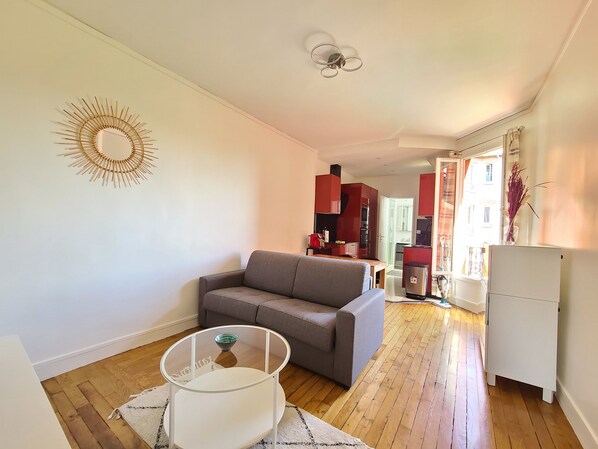 A living room with a grey sofa, a glass table, and a white refrigerator.