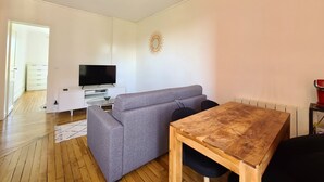 Ein modernes Wohnzimmer mit grauem Sofa, einem Holzesstisch, einem Flachbildfernseher auf einer weißen Kommode und einer Wanddekoration.