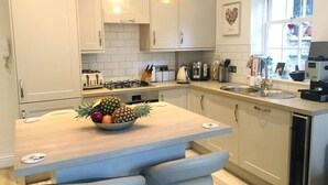 A modern kitchen with white cabinets, a central island with seating, a gas stove, and a coffee machine.